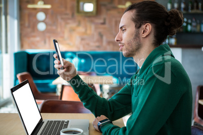 Man using mobile phone with laptop on table