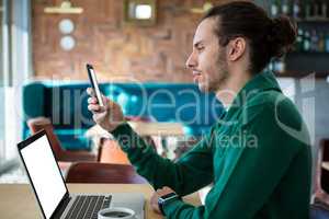 Man using mobile phone with laptop on table