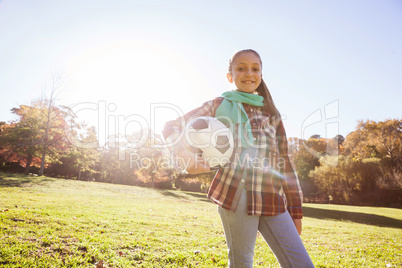 Low angle portrait of smiling girl holding soccer ball in park