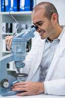 Smiling male optometrist looking through microscope