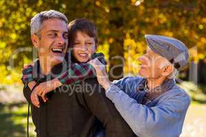Happy man piggybacking son while with father at park
