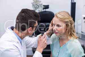 Optometrist examining female patient through ophthalmoscope