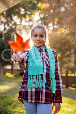 Portrait of happy girl showing autumn leaf at park