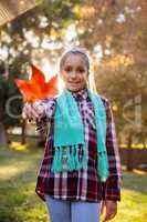 Portrait of happy girl showing autumn leaf at park
