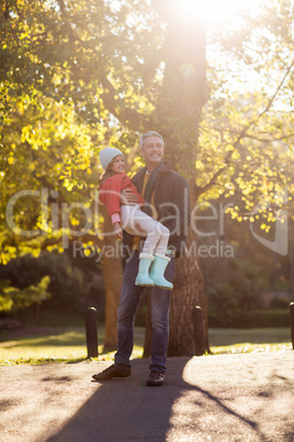 Father carrying daughter by autumn tree