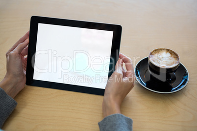 Woman using digital tablet with cup of coffee on table