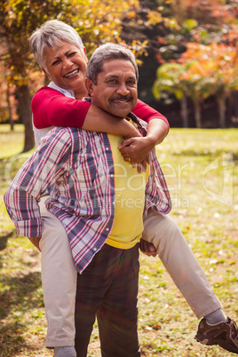 An elderly man carries his wife on his back