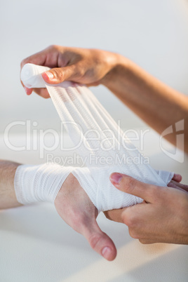 Physiotherapist putting bandage on male patient hand