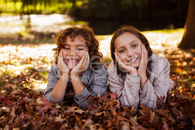 Portrait of happy siblings lying on autumn leaves