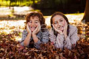 Portrait of happy siblings lying on autumn leaves