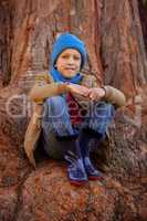 Portrait of smiling boy hugging knees while sitting on tree trun