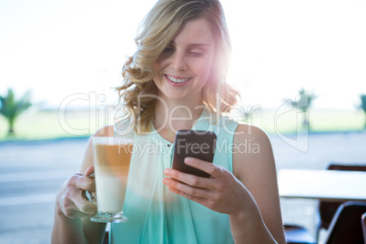 Smiling woman holding a coffee glass and using her mobile phone