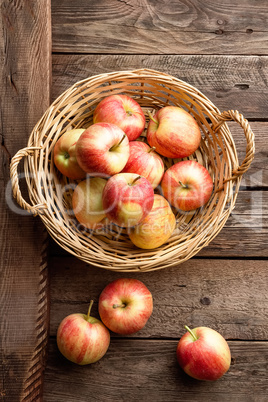 Fresh red apples in wicker basket on wooden table.