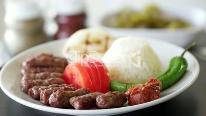 Turkish meatball inegol kofte with rice, onion, tomatoes and green pepper. Rotating shot. Slow motion.
