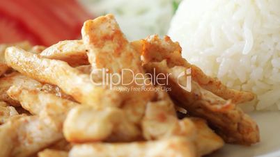 Grilled chicken rotating on plate with rice, green pepper, onion and tomatoes. Slow motion and close up shot.