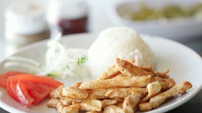 Grilled chicken rotating on plate with rice, green pepper, onion and tomatoes. Slow motion and close up shot.