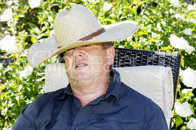 Man with straw hat has fallen asleep in the garden chair