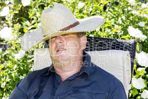 Man with straw hat has fallen asleep in the garden chair