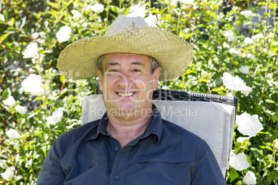 Cheerful man with straw hat in the garden chair