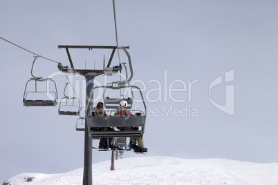 Snowboarders on chair-lift and ski slope at gray day