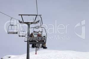 Snowboarders on chair-lift and ski slope at gray day