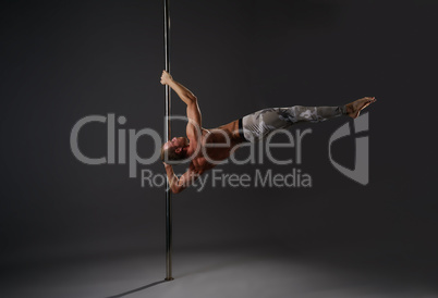 Strong gymnast exercising on pylon in studio