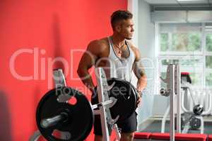 Handsome bodybuilder posing in gym with barbell