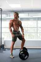 At gym. Bodybuilder poses with his foot on barbell