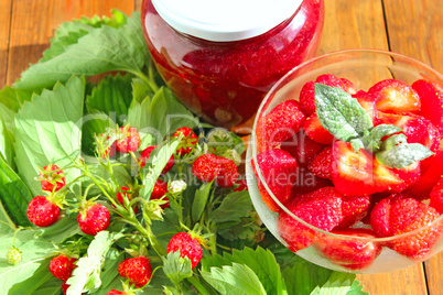 strawberries in transparent bowl and bunches with leaves