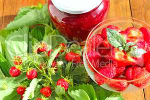 strawberries in transparent bowl and bunches with leaves