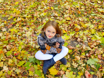 girl sits on the yellow leaves in the park