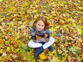 girl sits on the yellow leaves in the park