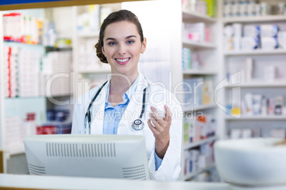 Smiling pharmacist holding medicine container in pharmacy