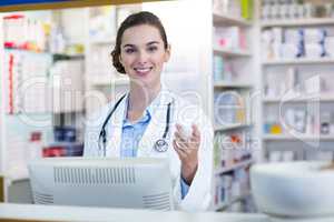 Smiling pharmacist holding medicine container in pharmacy