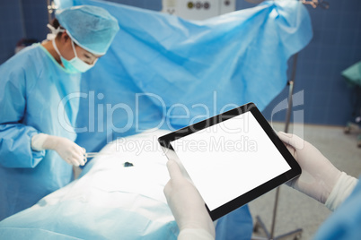 Surgeon using digital while nurse operating patient in operation