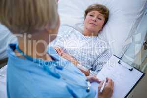 Nurse writing on clipboard while interacting with a patient