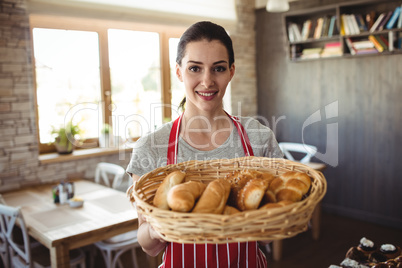 Portrait of female baker holding a basket of bread loafs