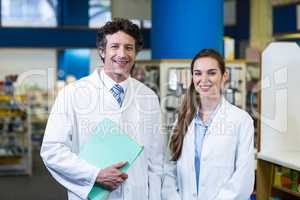 Smiling pharmacists standing with file in pharmacy