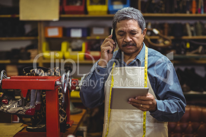 Shoemaker using digital tablet while talking on mobile phone