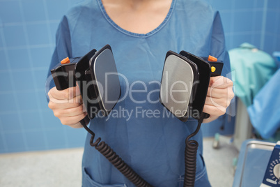 Mid section of female surgeon holding defibrillator