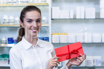 Smiling pharmacist holding present in pharmacy