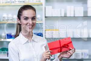 Smiling pharmacist holding present in pharmacy