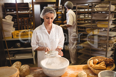 Female baker sifting flour through a sieve