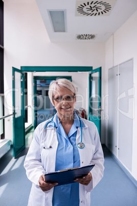 Confident female doctor with clipboard standing in hospital corr