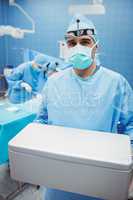 Portrait of surgeon holding ice box while colleagues performing