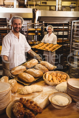 Male and female baker holding tray of loaf and michetta