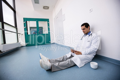Doctor sitting on floor and using digital tablet in corridor