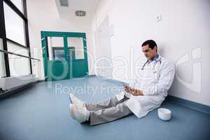 Doctor sitting on floor and using digital tablet in corridor