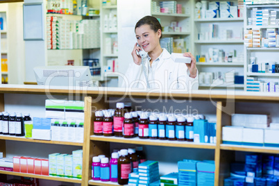 Pharmacist holding medicine box while talking on phone