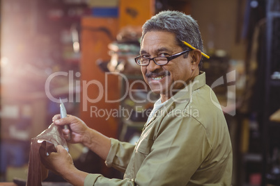 Portrait of smiling shoemaker cutting a piece of leather
